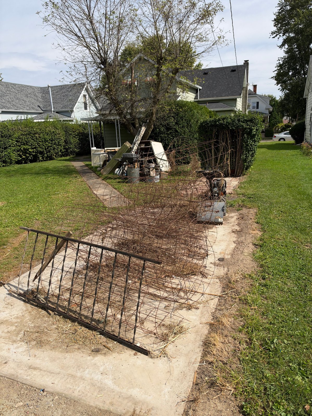Metal hay feeder and gate in residential yard with green lawn, trees, and house in background