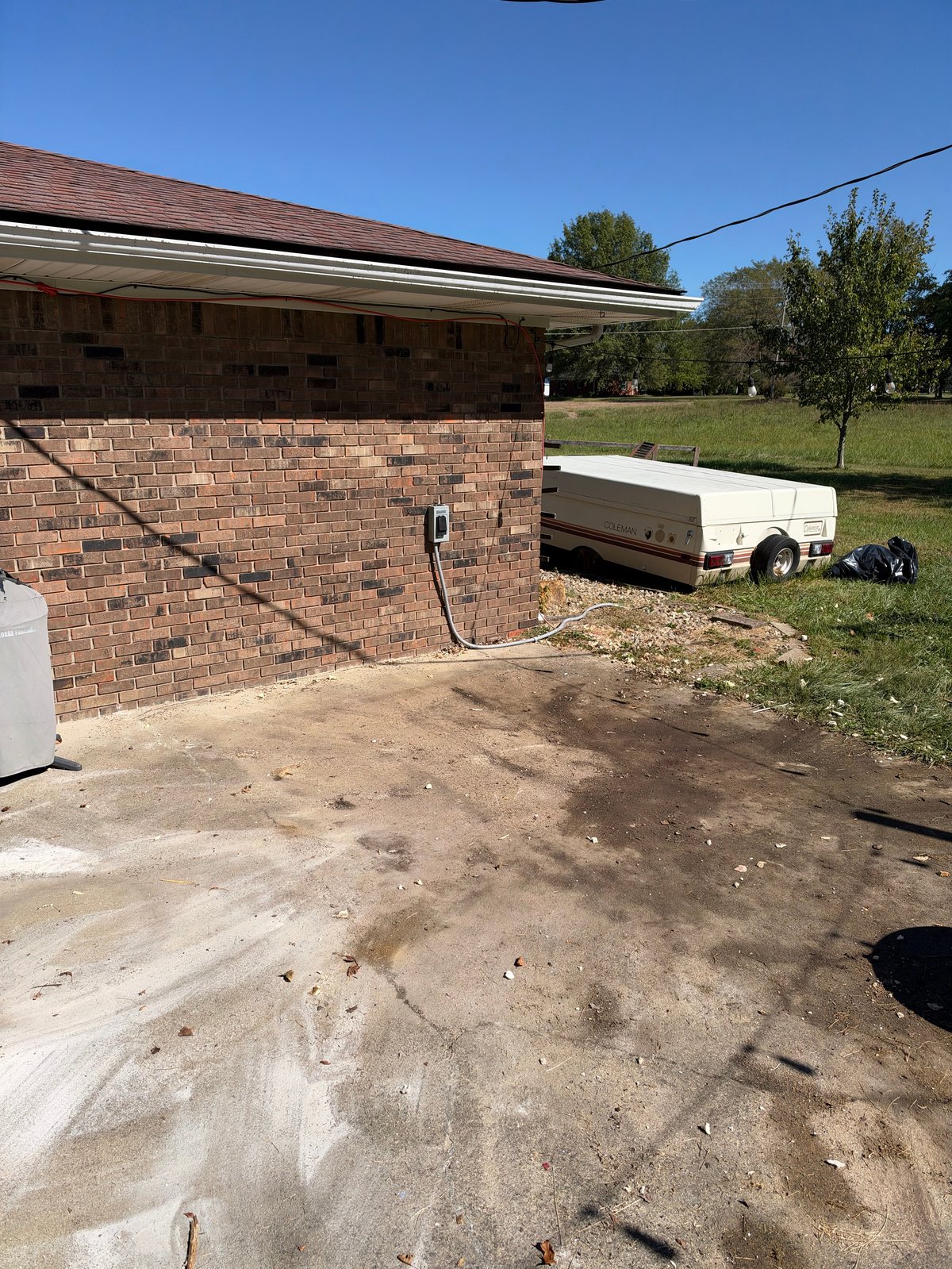 Brick garage with open door and white utility trailer parked on dirt ground under clear blue sky
