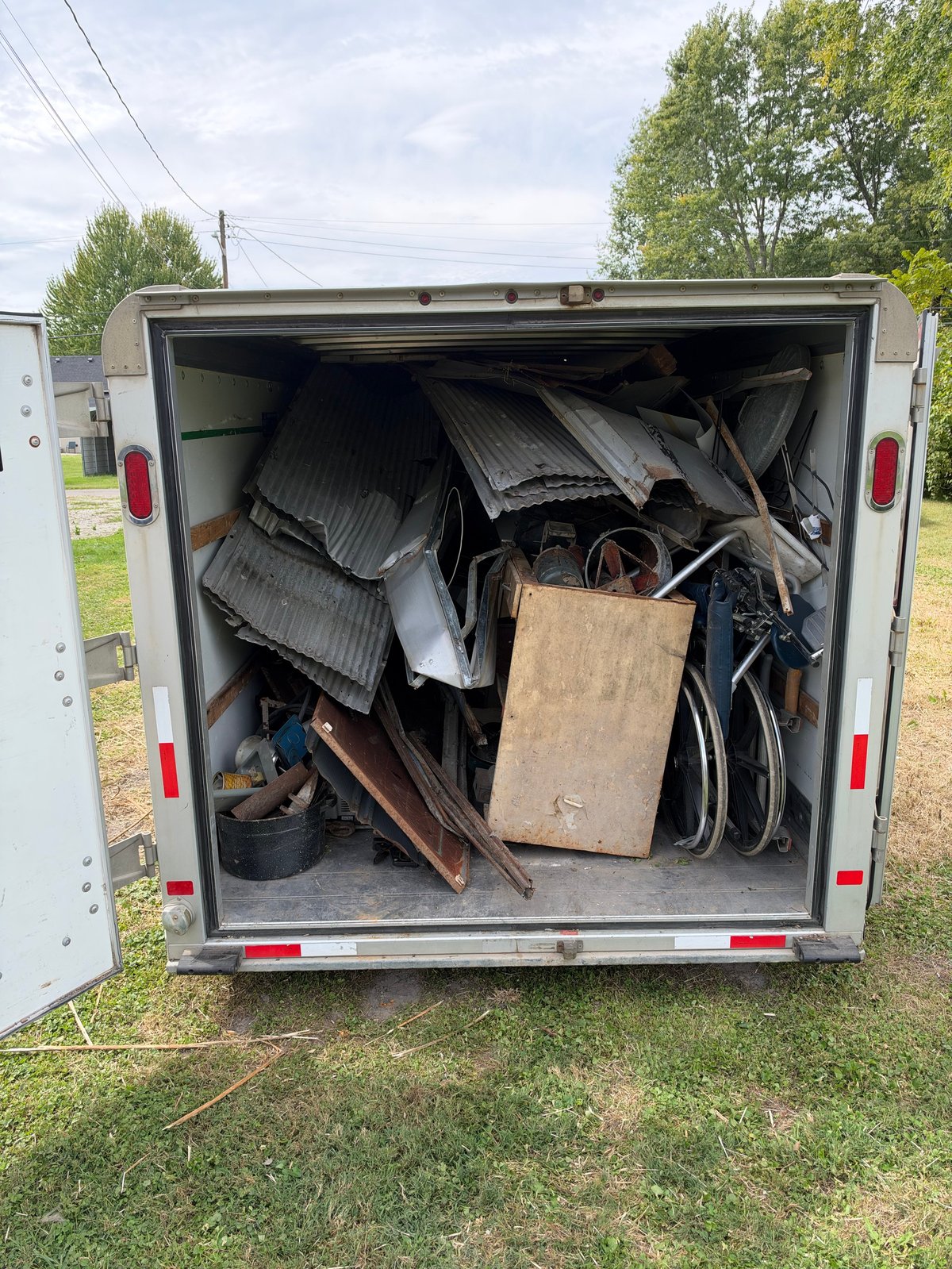 Open utility trailer filled with miscellaneous junk and scrap materials including metal sheets, wood, and various discarded items