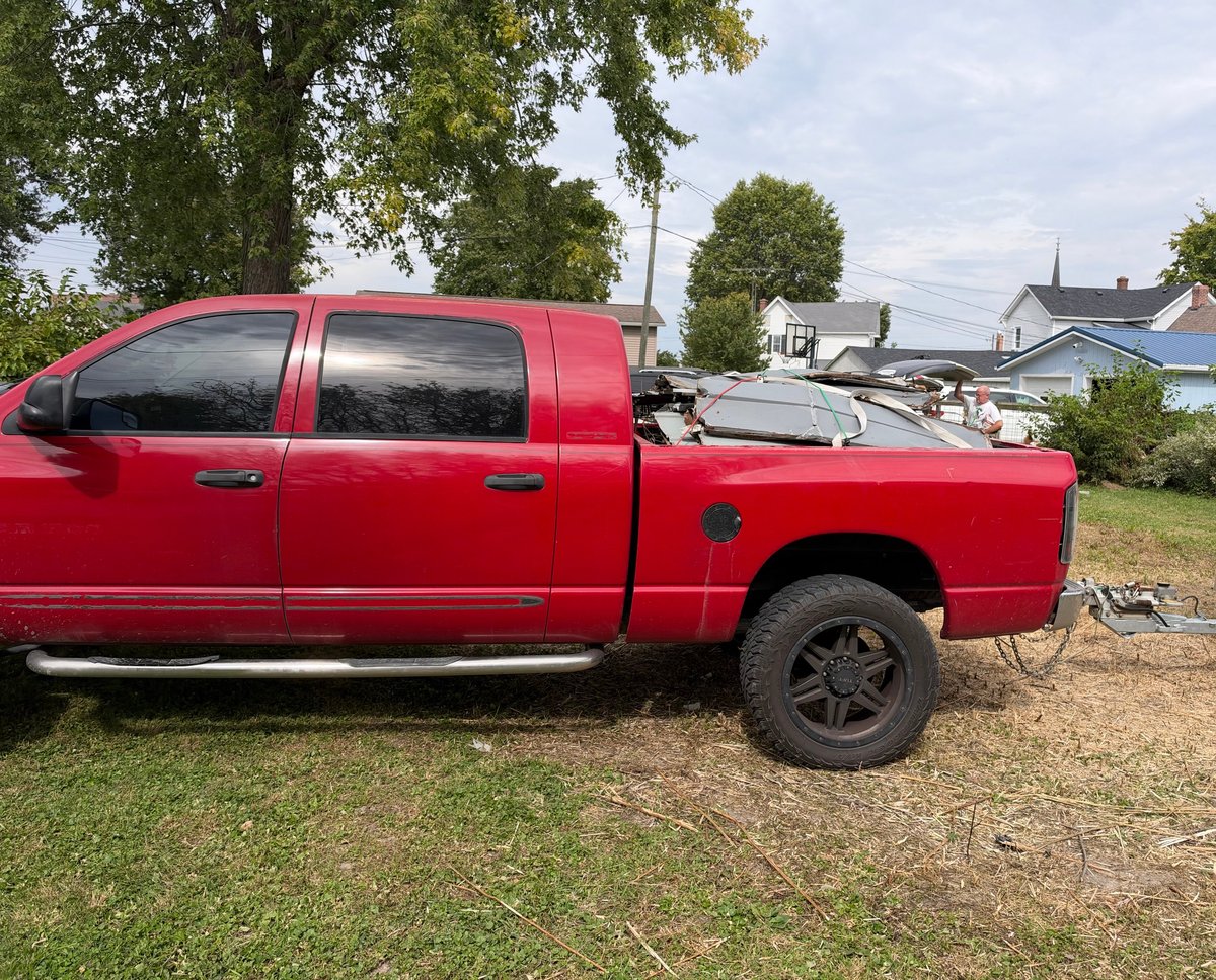 Red pickup truck parked on grassy area with trees and houses visible in background