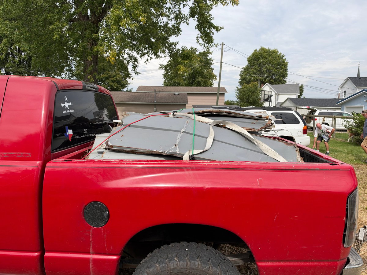 Red pickup truck bed viewed from the side with residential houses and trees in the background