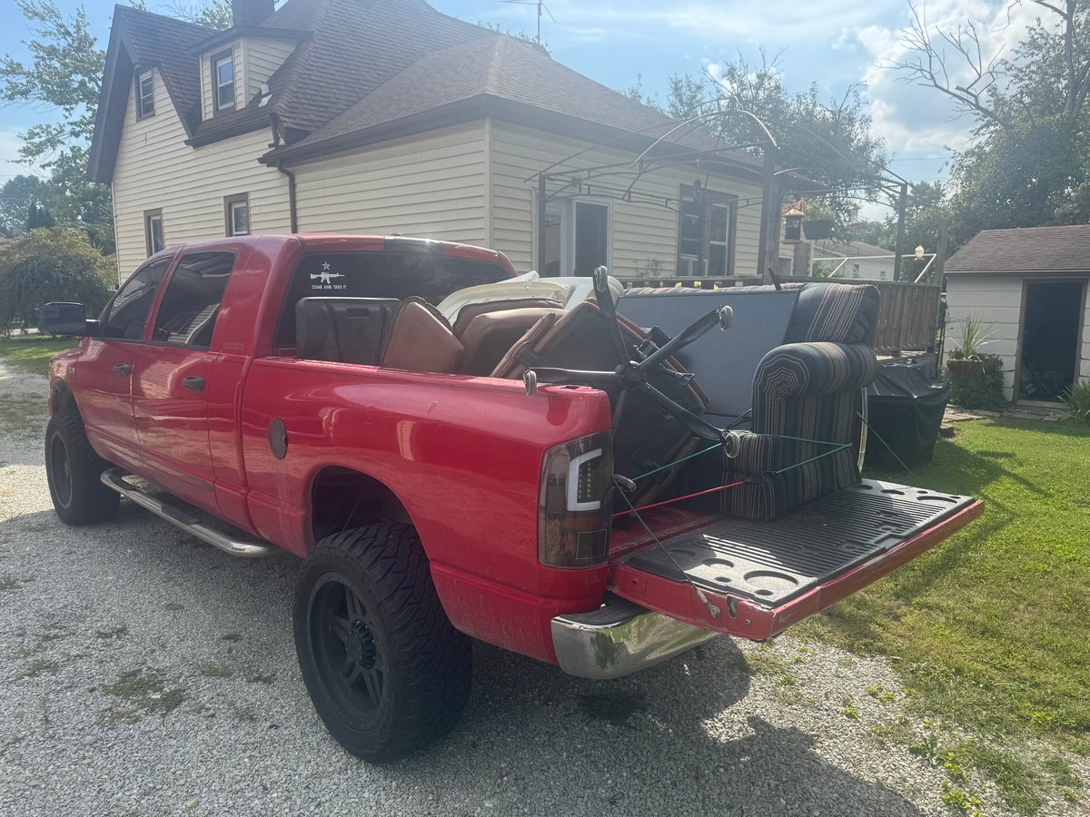 Red pickup truck with lowered tailgate carrying furniture in a residential driveway