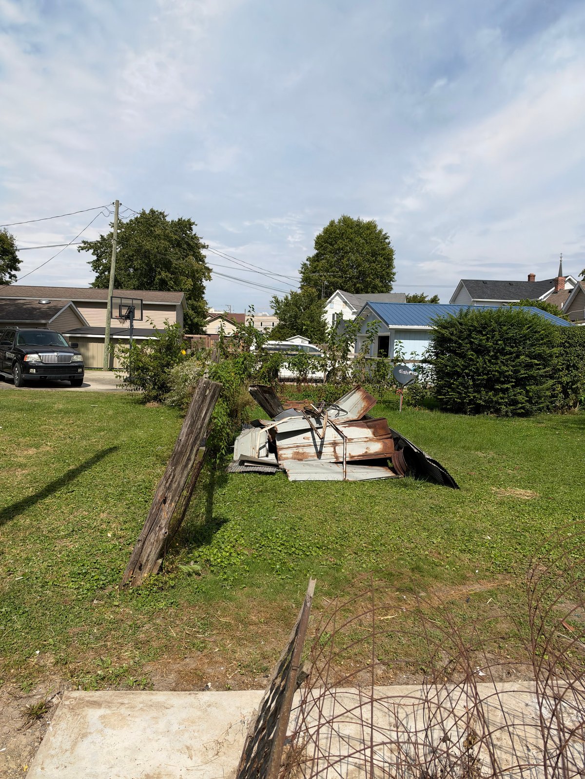 Rustic wooden log fence dividing a residential yard with lawn chairs and suburban houses in background